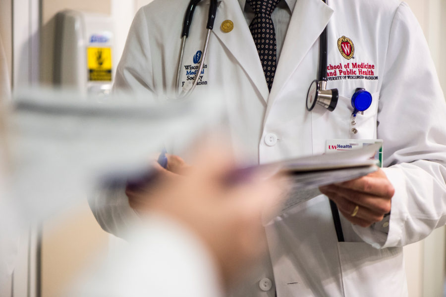 A close up of the embroidered W crest on a medical student's white coat as he speaks to a group of medical students