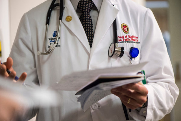 A close up of the embroidered W crest on a medical student's white coat as he speaks to a group of medical students