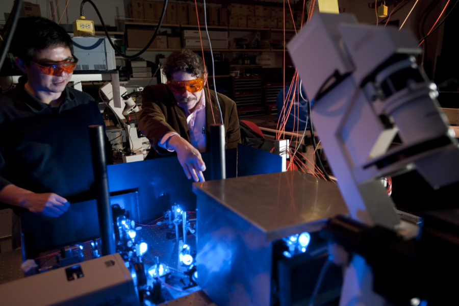 Shiguo Zhou (left) and David C. Schwartz look at the path that blue laser light follows through focusing optics and beam splitters