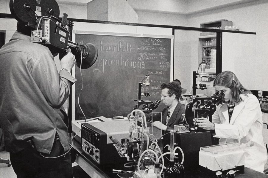 A man films Howard Temin, 1975 Nobel Prize in medicine and professor of oncology at the McArdle Laboratory, and a student at work in the lab.