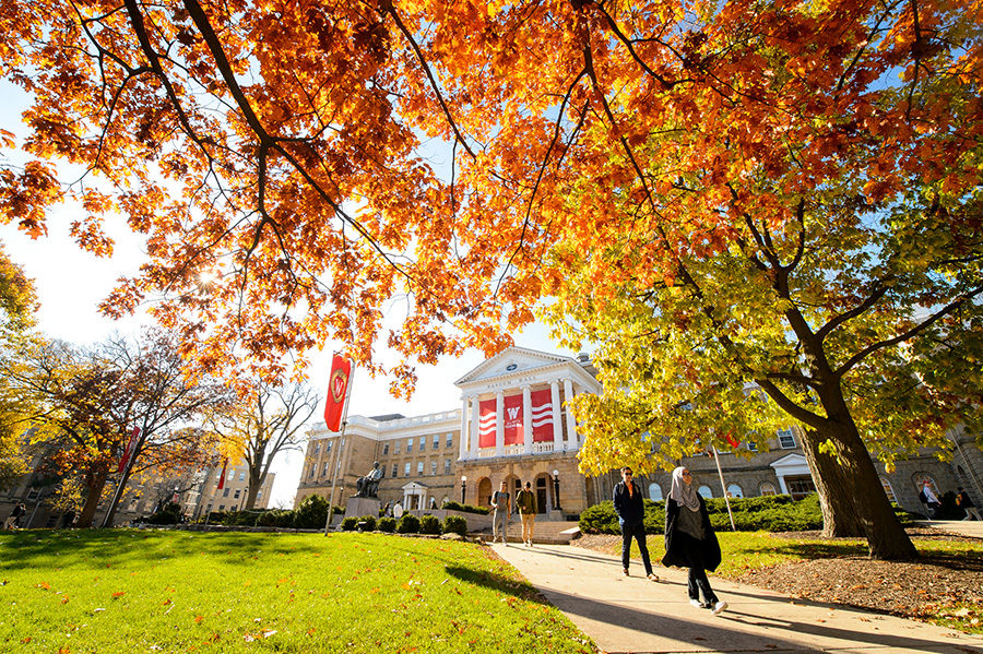 Students walk along a colorful tree-lined sidewalk outside Bascom Hall in fall at the University of Wisconsin-Madison