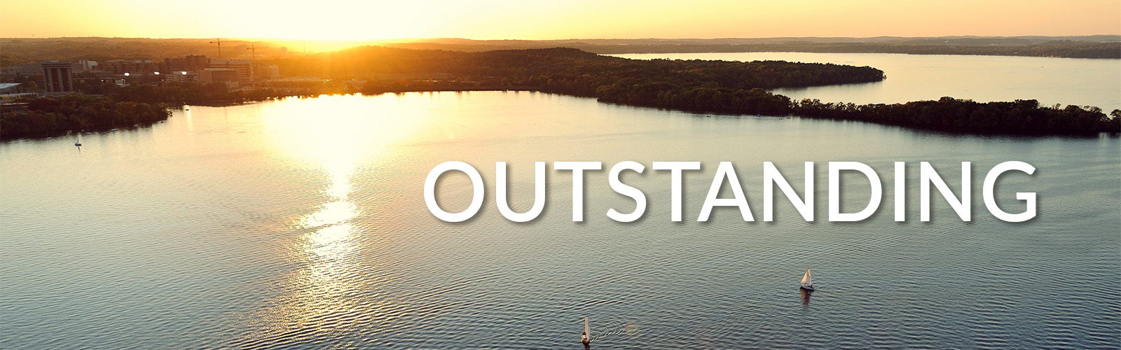 The word "Outstanding" is overlayed on a photo of sailboats dot Lake Mendota in an aerial view of the University of Wisconsin-Madison campus shoreline during an autumn sunset. On the horizon at right is a silhouette of Picnic Point, to the left is the medical campus.